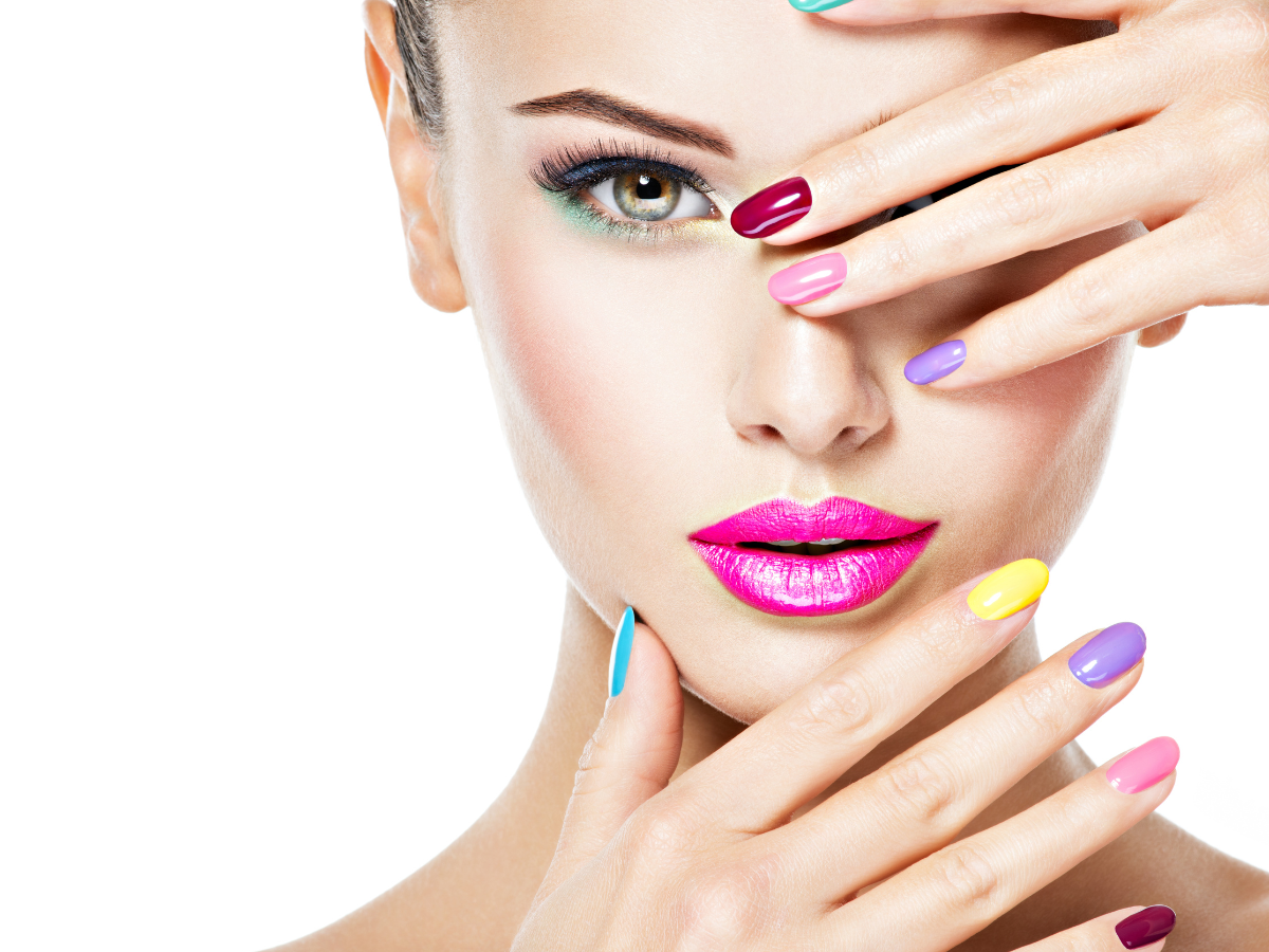 Cores de unhas para cada signo. Foto rosto de uma mulher branca com as mãos sobre ele e unhas coloridas. Batom rosa.